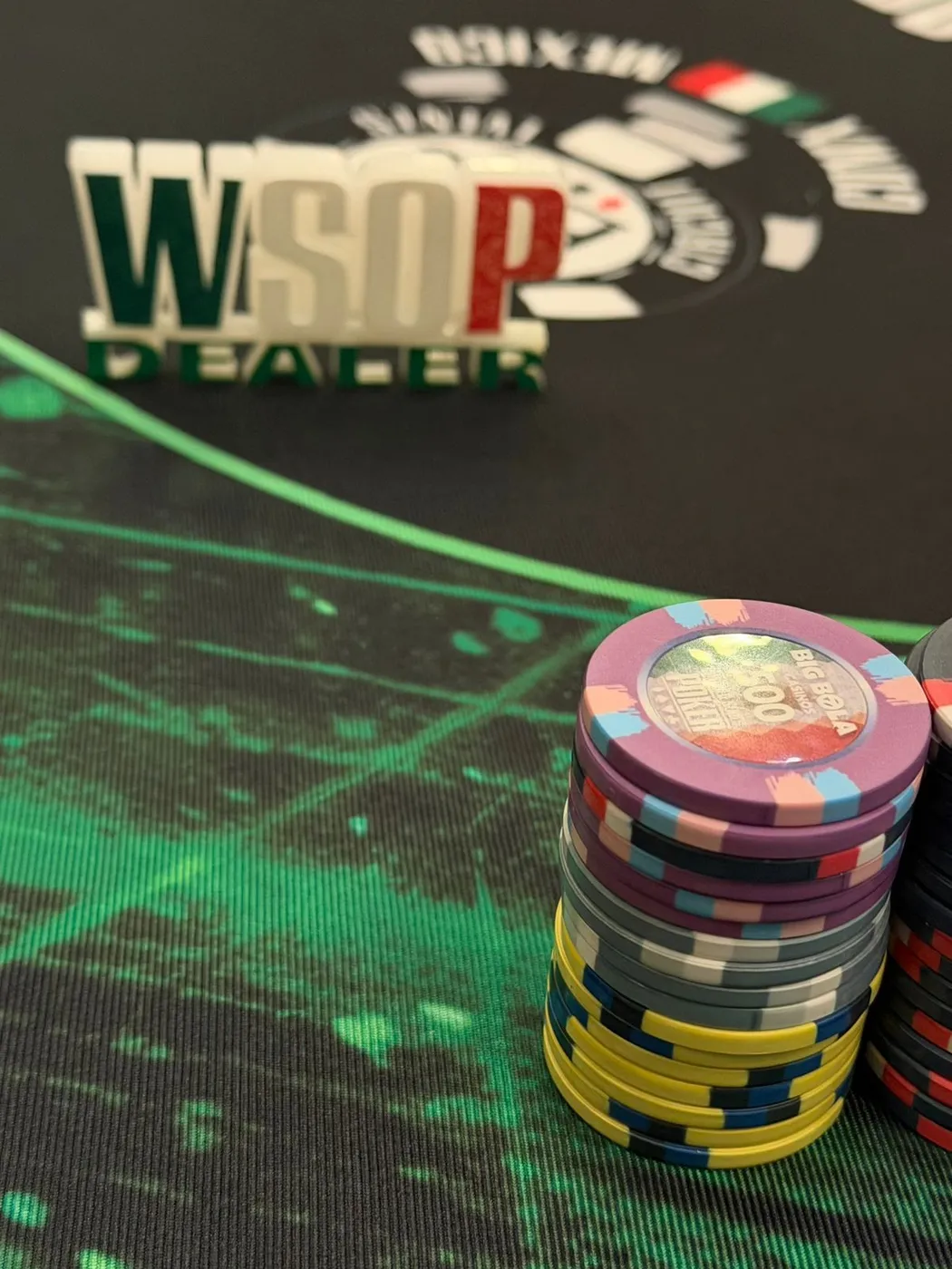 Botón de dealer de la WSOP junto a una torre de fichas de Big Bola sobre el tapete